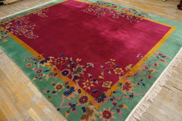 Lustrous magenta rug with a wide floral green border and gold trim rests on worn wooden flooring.