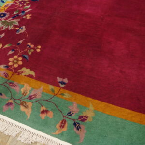 Floral rug with a magenta field, teal border, and gold stripe, resting on rustic wood floors.