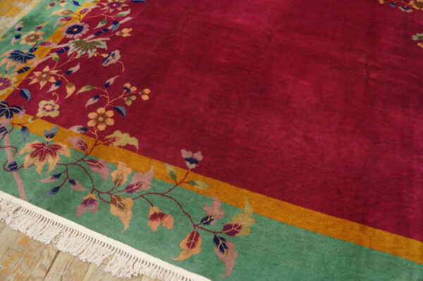 Floral rug with a magenta field, teal border, and gold stripe, resting on rustic wood floors.