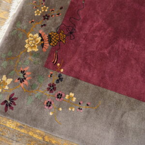 High-pile rug detail showing a gray floral border meeting a solid burgundy field on distressed wood.