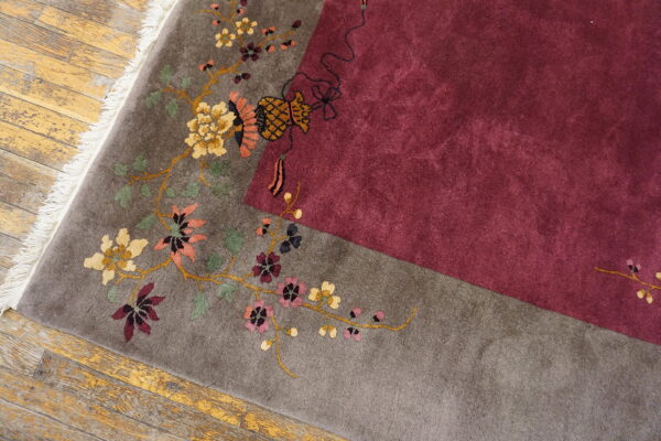 High-pile rug detail showing a gray floral border meeting a solid burgundy field on distressed wood.