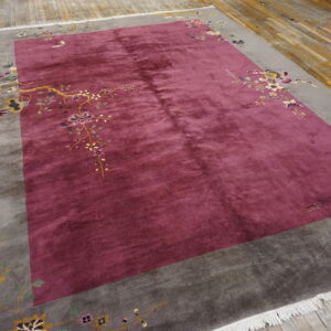 Lustrous burgundy rug with a gray border decorated by delicate floral branches on plank wood flooring.