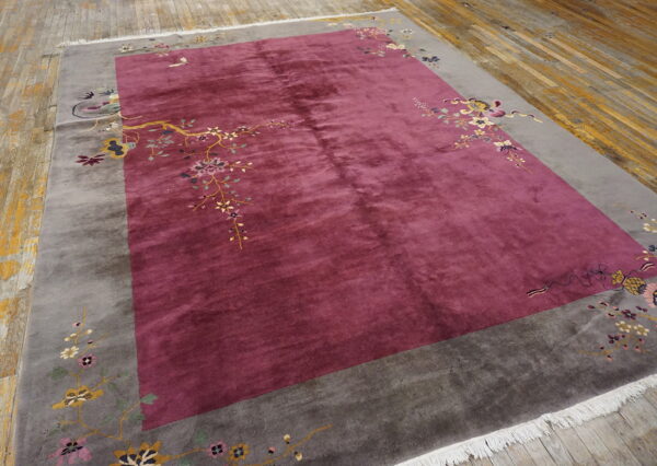 Lustrous burgundy rug with a gray border decorated by delicate floral branches on plank wood flooring.