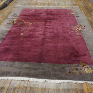 Maroon rug with a gray border and corner floral patterns rests on distressed plank flooring.