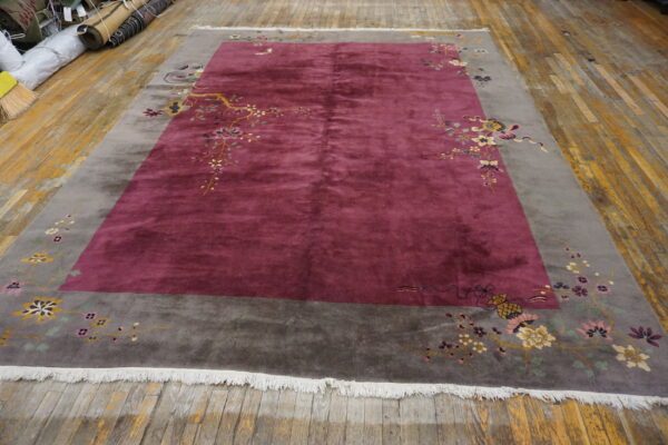 Maroon rug with a gray border and corner floral patterns rests on distressed plank flooring.