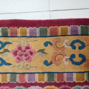 Multicolored rug featuring a yellow field with pink floral designs, blue scrolls, and a vibrant scalloped border.