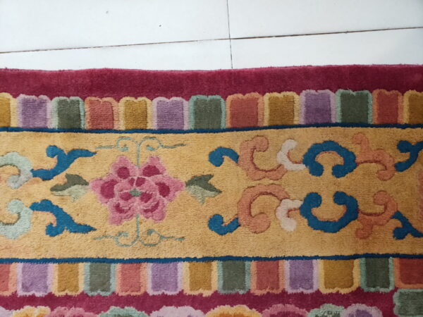 Multicolored rug featuring a yellow field with pink floral designs, blue scrolls, and a vibrant scalloped border.