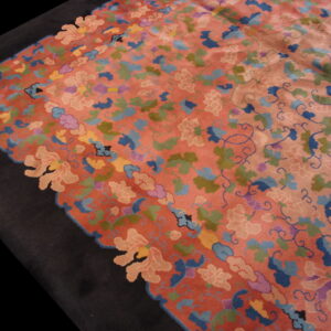 Multicolored floral rug in coral and pink with blue and green designs, bordered by solid dark black.