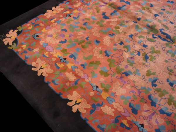 Multicolored floral rug in coral and pink with blue and green designs, bordered by solid dark black.