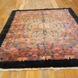Multicolor floral rug with a salmon field and black border displayed on polished wood plank flooring.