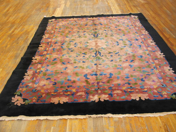 Multicolor floral rug with a salmon field and black border displayed on polished wood plank flooring.