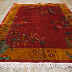 High-pile red and gold rug featuring detailed floral motifs and vases, displayed on wood flooring.