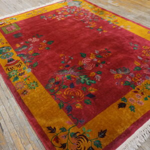 Deep red rug with gold border and elaborate floral patterns rests on distressed wooden planks.