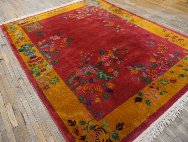 Deep red rug with gold border and elaborate floral patterns rests on distressed wooden planks.