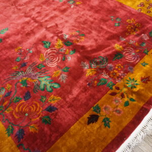 Close-up of a plush red rug with yellow borders and multicolor scrolling floral and bird motifs.