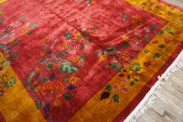Close-up of a plush red rug with yellow borders and multicolor scrolling floral and bird motifs.