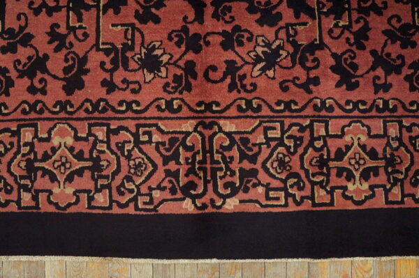 A close-up of a high-pile rug border in rust, black, and beige, over light wooden flooring.