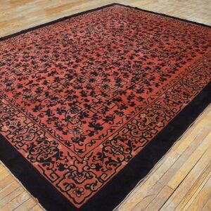 A large red-orange rug with black stylized motifs and border is laid upon wood floorboards.