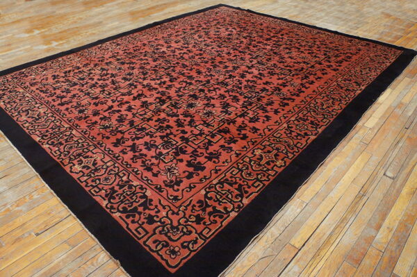 A large red-orange rug with black stylized motifs and border is laid upon wood floorboards.