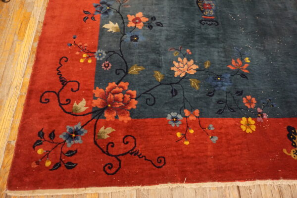 Deep blue floral rug border in rust red on yellow wooden floorboards.