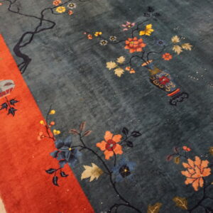 Teal rug with ornate orange, blue, and yellow flowers, a vase motif, and a wide red-orange border.