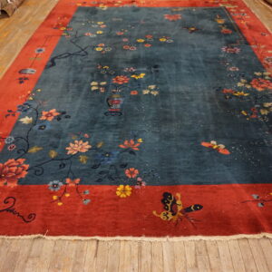 Teal rug with a coral red border displays scattered flowers, vines, and butterflies on wooden floorboards.
