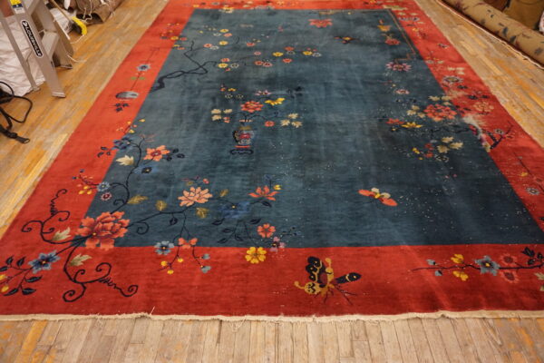 Teal rug with a coral red border displays scattered flowers, vines, and butterflies on wooden floorboards.