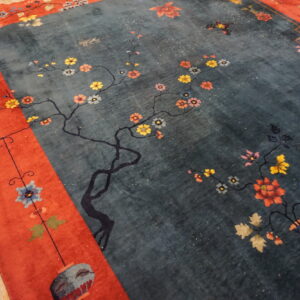 Dark teal rug with multicolored floral branch motifs and a bold orange-red decorative border.