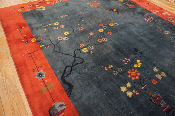 Dark teal rug with multicolored floral branch motifs and a bold orange-red decorative border.