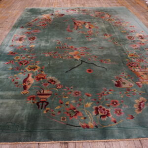 A high-pile teal rug featuring ornate pink and red flowers and a geometric border on wood planks.
