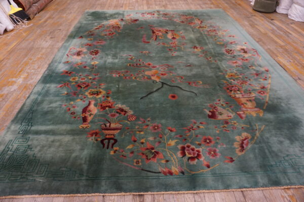 A high-pile teal rug featuring ornate pink and red flowers and a geometric border on wood planks.