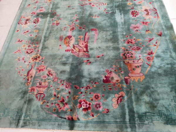 Distressed teal rug with rose and peach floral sprays lies on a bright, white tile floor.
