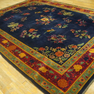 Navy rug featuring colorful floral patterns, thick red and green borders, displayed on light wood flooring.