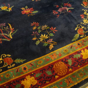 A navy rug with scattered florals and a wide red and green ornamental border rests on wood flooring.
