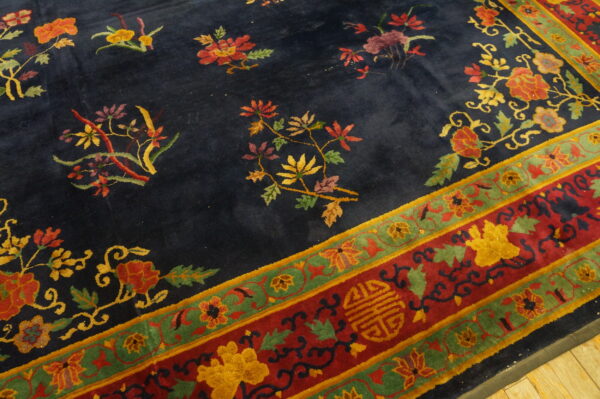 A navy rug with scattered florals and a wide red and green ornamental border rests on wood flooring.