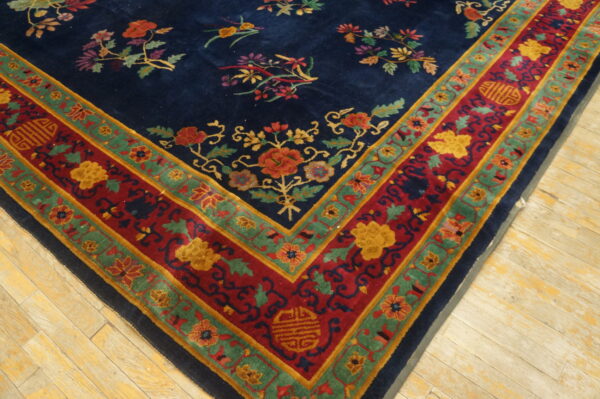 A detailed blue rug with multicolored floral sprays and a wide red and green border rests on pale wood.