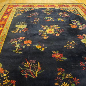 Large navy rug with scattered colorful floral sprays and ornate red and green borders rests on wood floorboards.