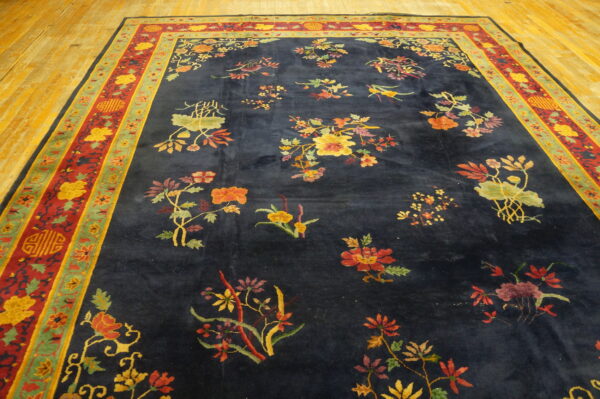 Large navy rug with scattered colorful floral sprays and ornate red and green borders rests on wood floorboards.