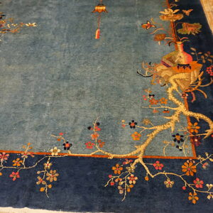 High-pile dusty blue rug with navy border, featuring gold floral vines, rests on light hardwood floors.