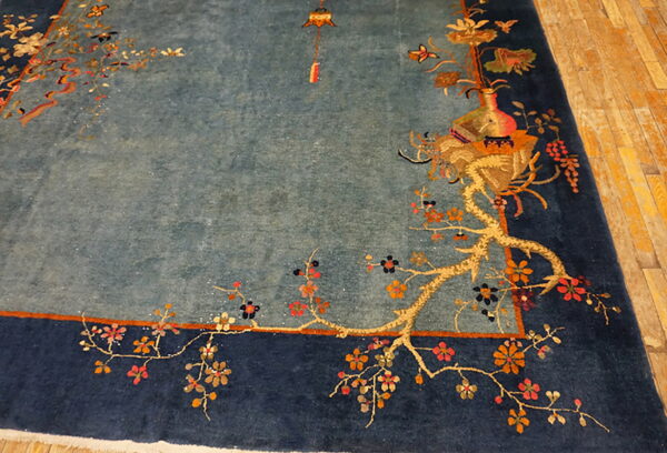 High-pile dusty blue rug with navy border, featuring gold floral vines, rests on light hardwood floors.
