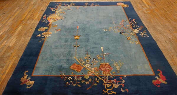 Light blue and indigo rug featuring ornate motifs and symbols rests on light brown plank flooring.