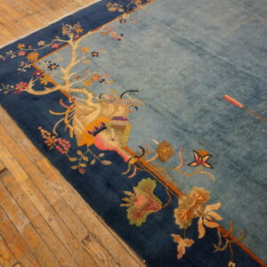 Light blue rug featuring a flowering branch design and dark blue border on worn hardwood planks.