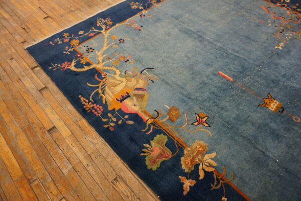 Light blue rug featuring a flowering branch design and dark blue border on worn hardwood planks.