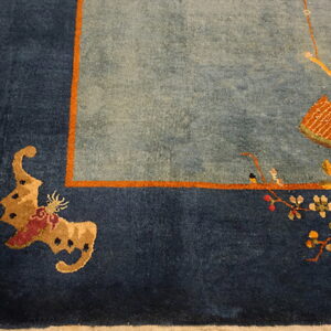 Patterned blue and orange rug with a floral design and dark border rests on distressed wooden floorboards.