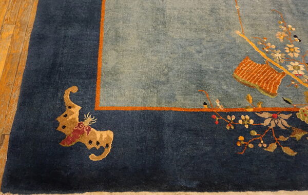 Patterned blue and orange rug with a floral design and dark border rests on distressed wooden floorboards.