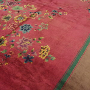 Magenta rug featuring blue, yellow, and green floral designs and a broad tan border with green stripes.