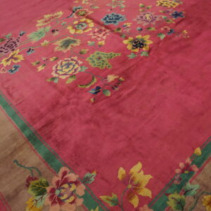 A magenta field rug with colorful floral vines and a wide taupe border lies on distressed wood flooring.