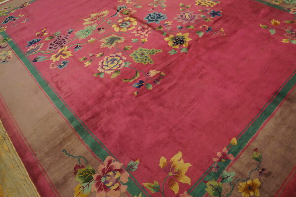 A magenta field rug with colorful floral vines and a wide taupe border lies on distressed wood flooring.
