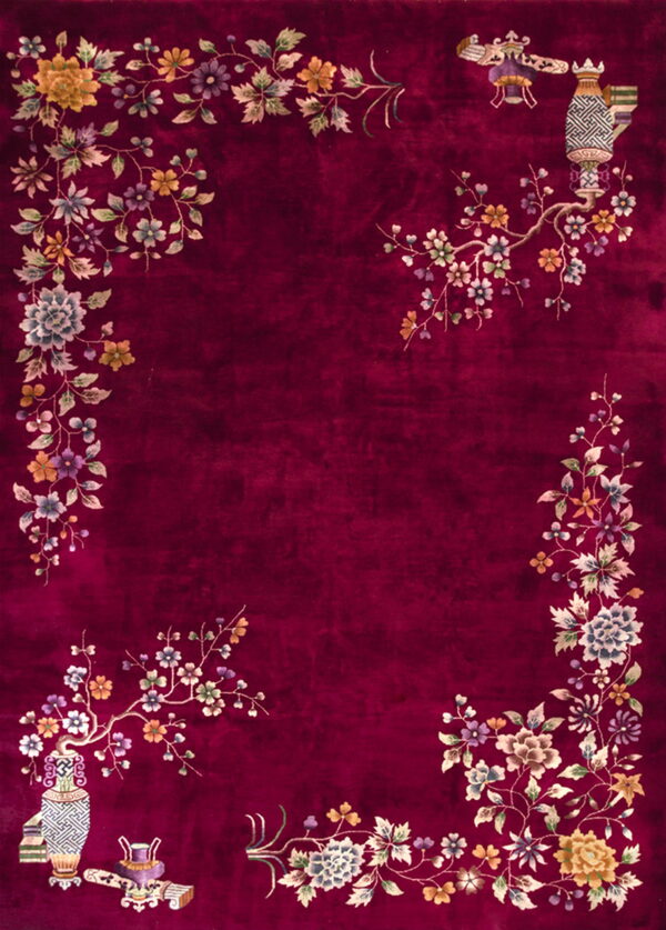 A deep maroon rug with an elaborate multicolored floral border and corner motifs, including vases and lanterns.