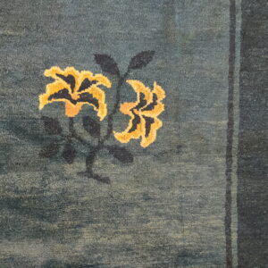 Low-pile teal rug detail showing yellow floral motifs, dark stems, and vertical navy stripes along the right edge.